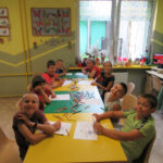 Dzieci siedzą przy stolikach i kolorują kredkami ołówkowymi łapacze snów.