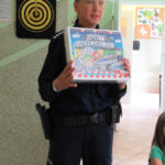 Policjantka w mundurze prezentuje grę planszową “Zostań dzielnicowym”