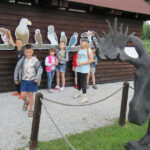 Grupa dzieci przy tablicy z naturalnej wielkości ptakami z Puszczy Białowieskiej, obok figura łosia