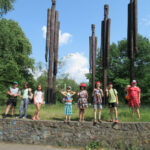 Grupa dzieci pozuje na tle wysokich, drewnianych rzeźb